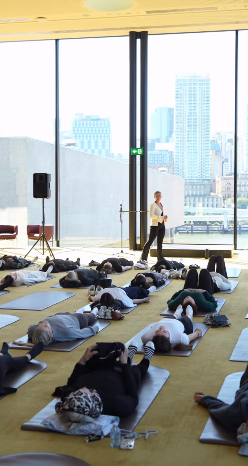 Sharleen leading a corporate breathwork session in a light-filled room overlooking the city